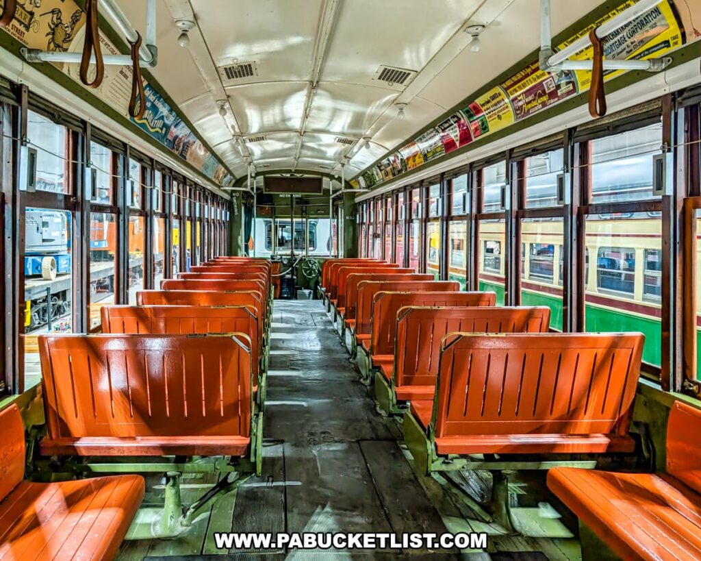 Interior view of a historic trolley car at the Pennsylvania Trolley Museum in Washington County, Pennsylvania, featuring rows of polished wooden bench seats, vintage advertisements above the windows, and hand straps for standing passengers.