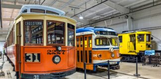 Trio of vintage trolleys on display inside the Trolley Display Building at the Pennsylvania Trolley Museum in Washington County, Pennsylvania, including an orange Crosstown car, a blue and orange Media car, and a yellow maintenance trolley.