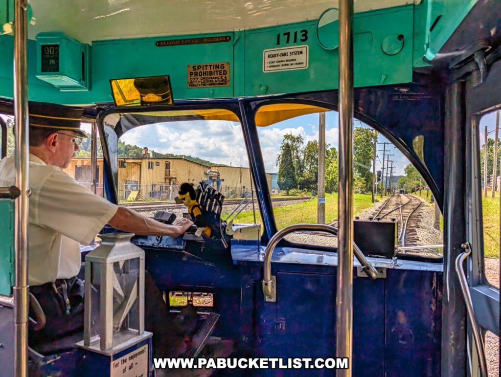 Motorman operating a vintage trolley at the Pennsylvania Trolley Museum in Washington County, Pennsylvania, with a view through the front windows of the tracks curving ahead on a sunny day.
