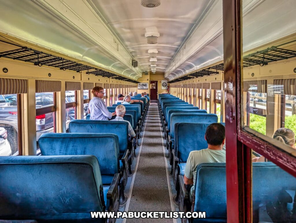 Passengers sit and chat inside a vintage Stourbridge Line railcar with blue cushioned seats, overhead luggage racks, and large windows during a sightseeing excursion in Honesdale, Wayne County, Pennsylvania.