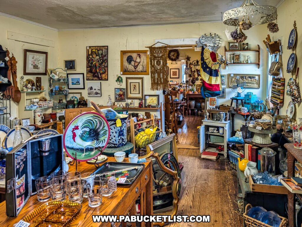 Second-floor room at Wexford General Store Antiques in Allegheny County, PA filled with an eclectic mix of vintage glassware, rooster-themed kitchenware, framed artwork, patriotic textiles, and decorative collectibles displayed on wooden tables and shelves.