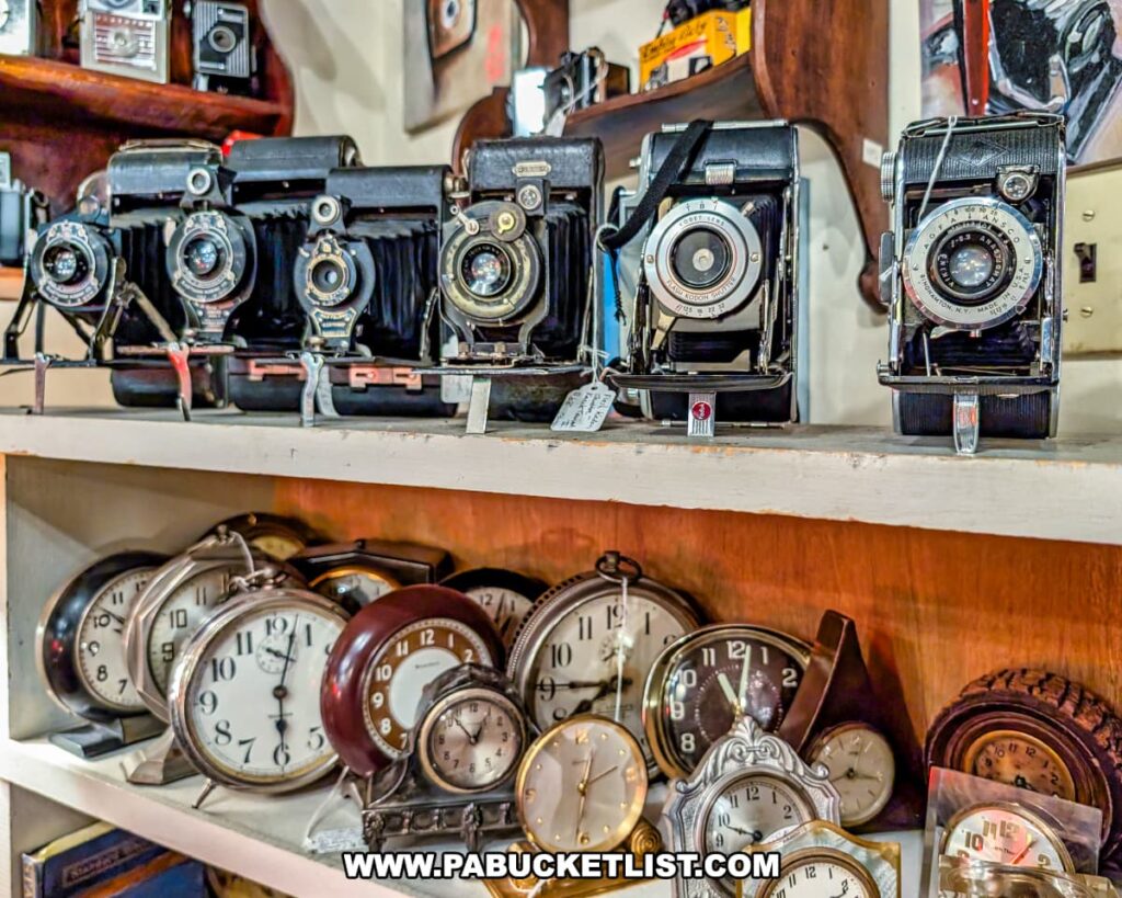 Display of vintage cameras and antique alarm clocks at Wexford General Store Antiques in Allegheny County, PA, showcasing a collection of early 20th-century folding cameras on the top shelf and an assortment of classic timepieces on the shelf below.