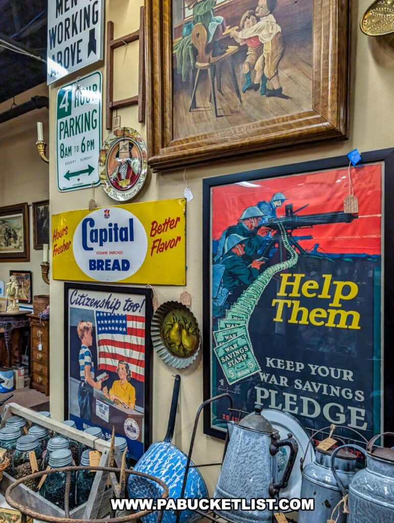 Wall display at the Antique Center of Strabane in Canonsburg, Pennsylvania, featuring vintage advertising signs, World War II-era posters, framed artwork, enamelware pitchers, and assorted collectibles from the early to mid-20th century.