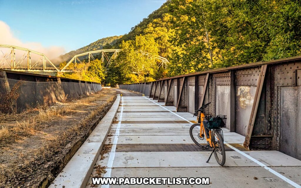 Yellow bicycle resting on the Mahoning Creek Railroad Bridge along the Armstrong Trail in western Pennsylvania, with the steel truss road bridge and forested hills visible in the background on a clear morning.