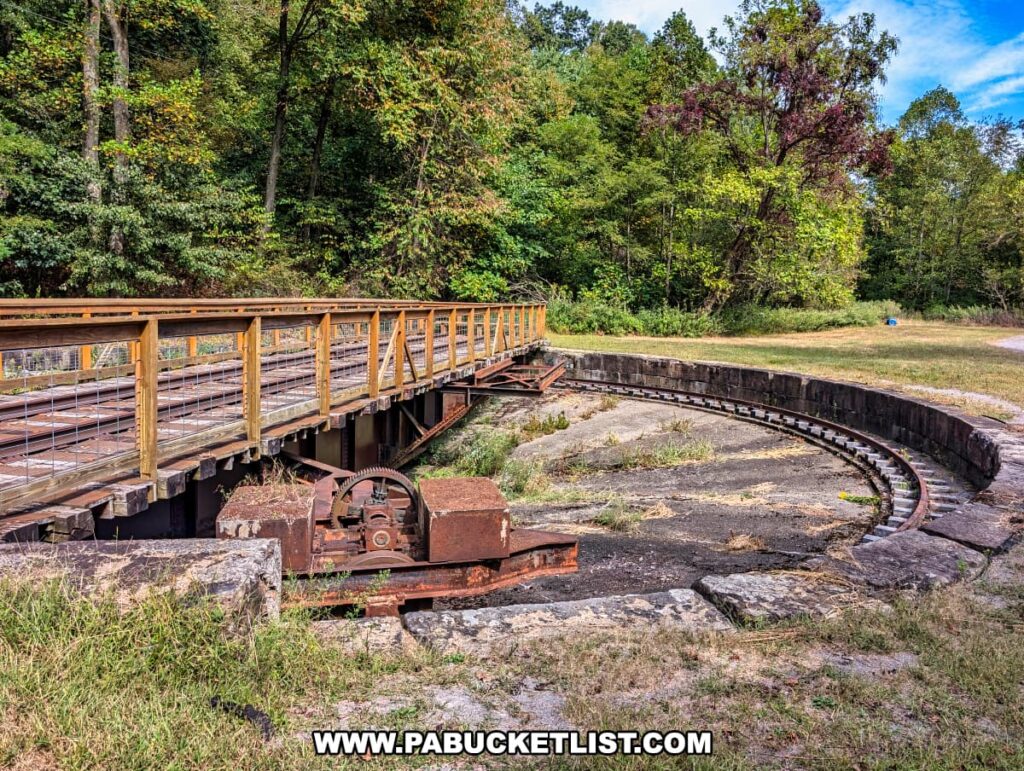 Historic railroad turntable at Phillipston along the Armstrong Trail in western Pennsylvania, featuring rusted gears, circular stonework, and wooden decking surrounded by trees and grassy clearings.