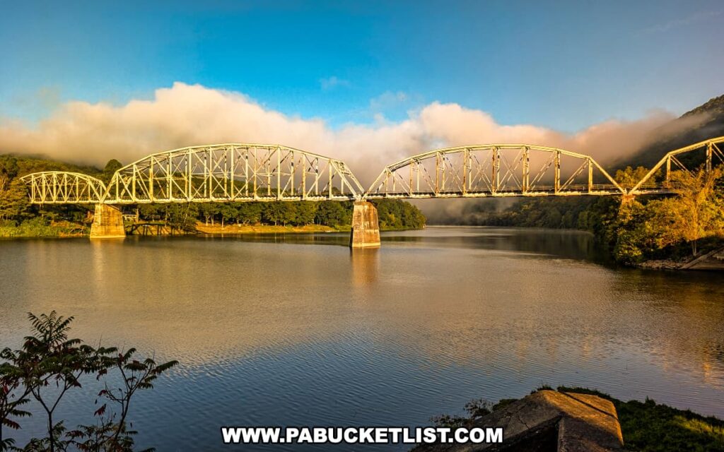 Sunrise view of the historic Pittsburgh and Shawmut Railroad Bridge spanning the Allegheny River along the Armstrong Trail in western Pennsylvania, with soft morning fog clinging to the surrounding hills.