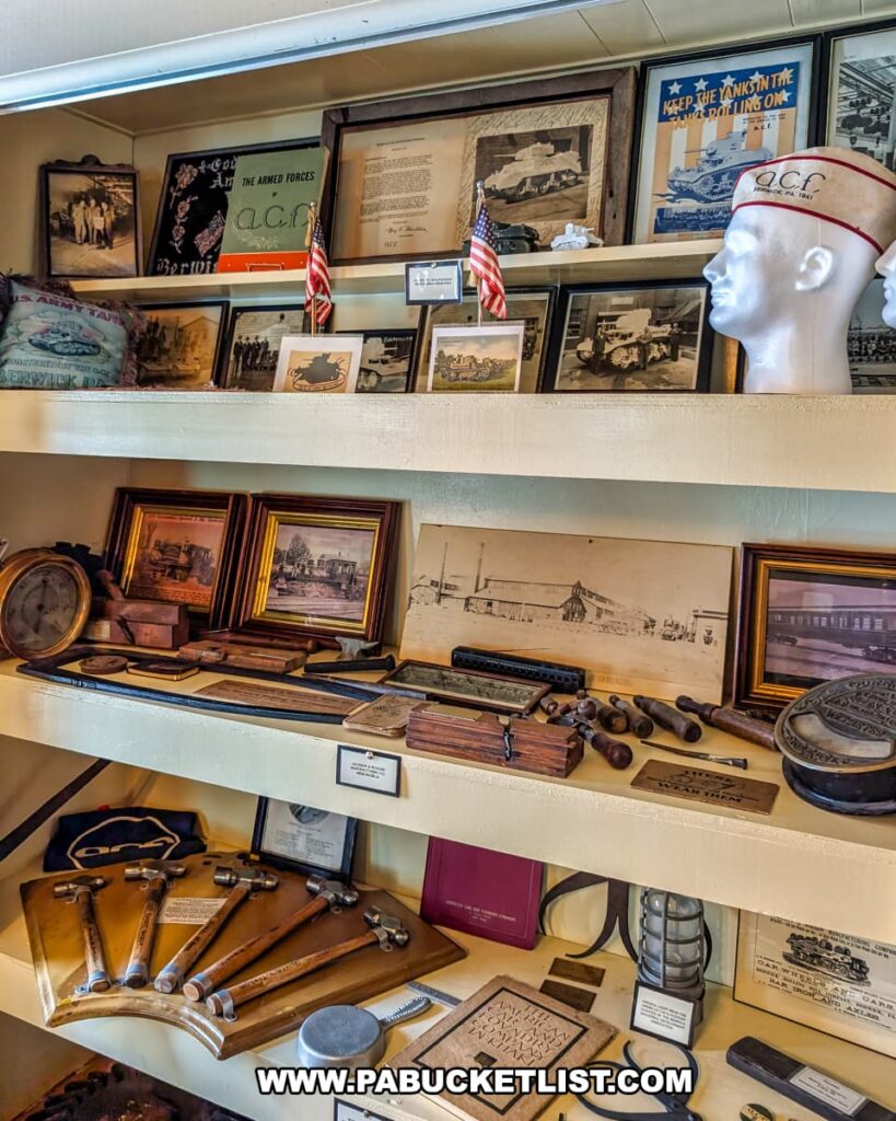 Display of American Car and Foundry memorabilia at the Berwick Historical Society Museum in Columbia County, PA, featuring vintage photographs, patriotic posters, factory tools, nameplates, military artifacts, and framed illustrations highlighting the company’s role in Berwick’s industrial and wartime history.