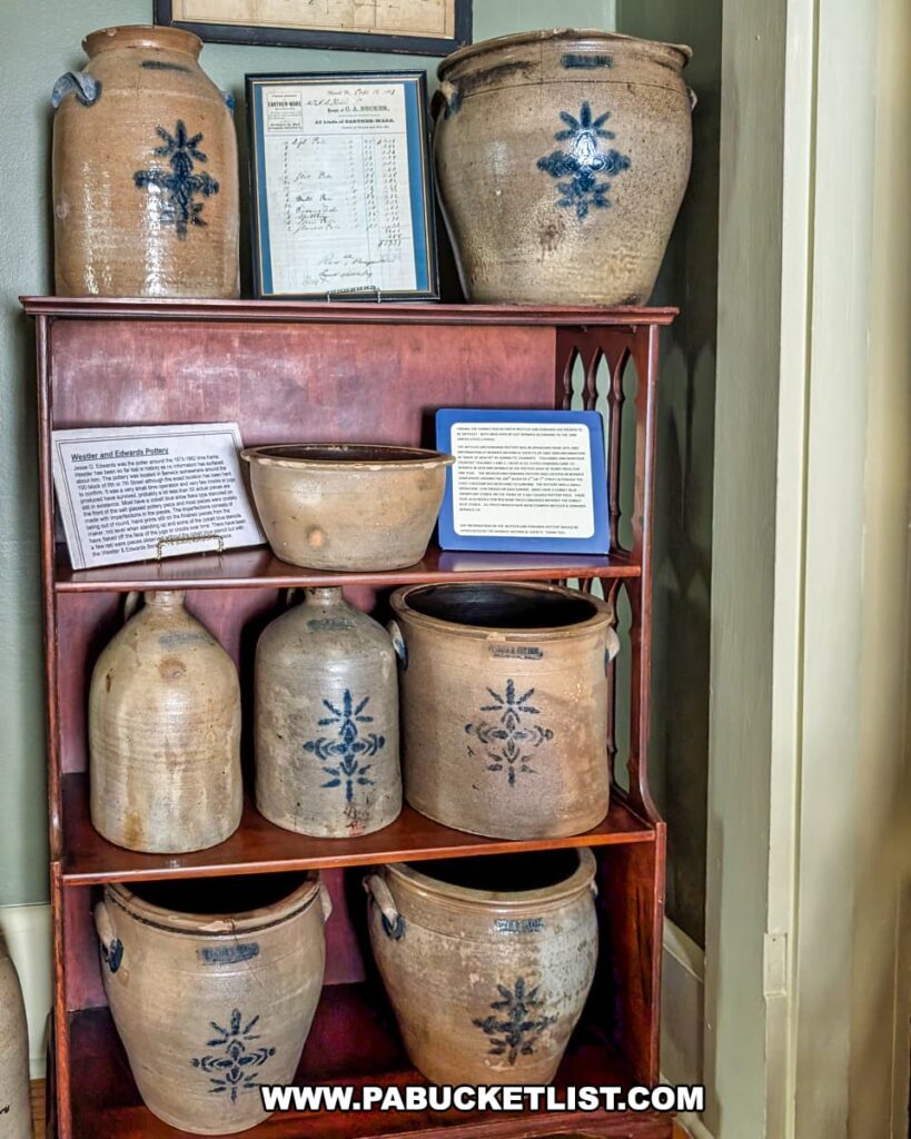 Display of 19th-century stoneware pottery at the Berwick Historical Society Museum in Columbia County, PA, featuring handcrafted jugs and crocks with cobalt blue floral designs, along with historical documents and interpretive signs detailing local pottery makers and their contributions to the community’s heritage.