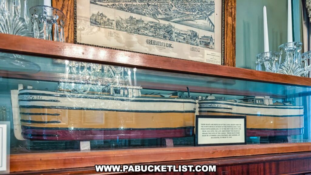 Display case at the Berwick Historical Society Museum in Columbia County, PA, featuring a detailed model of a canal boat once used on the North Branch Division of the Pennsylvania Canal, with a historic map of Berwick hanging above and crystal candlesticks on either side.