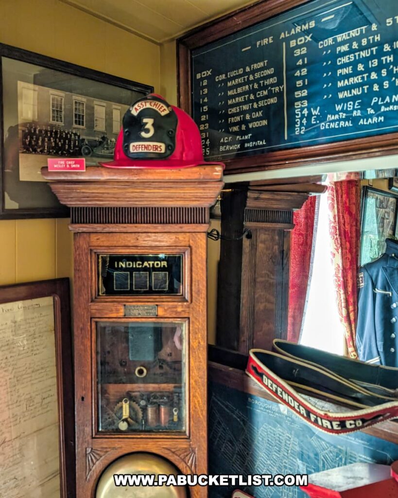 Vintage fire company memorabilia on display at the Berwick Historical Society Museum in Columbia County, PA, featuring an antique fire alarm indicator box, a red fire chief’s helmet, historic photographs, and a Defenders Fire Company parade hat.