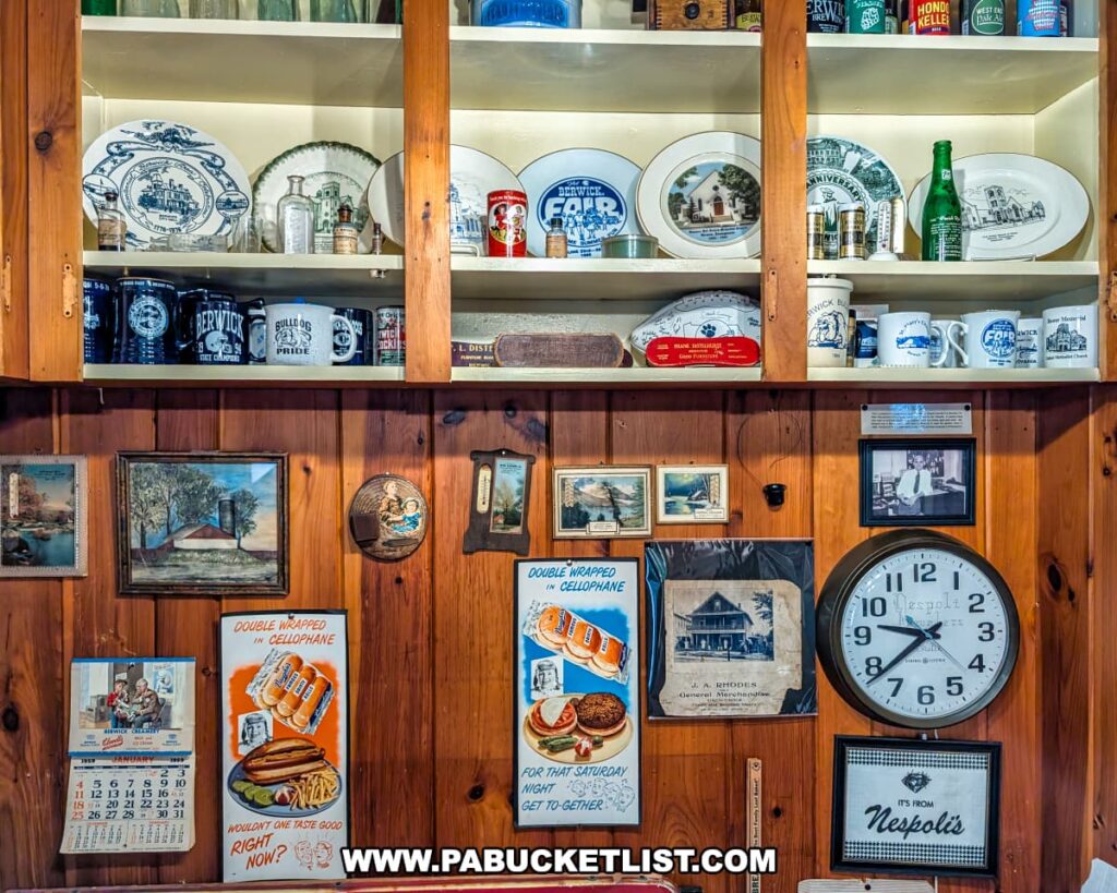 Display of vintage Berwick business memorabilia at the Berwick Historical Society Museum in Columbia County, PA, featuring old advertising signs, collectible mugs, commemorative plates, historic calendars, glass bottles, and photographs celebrating local businesses and community history.