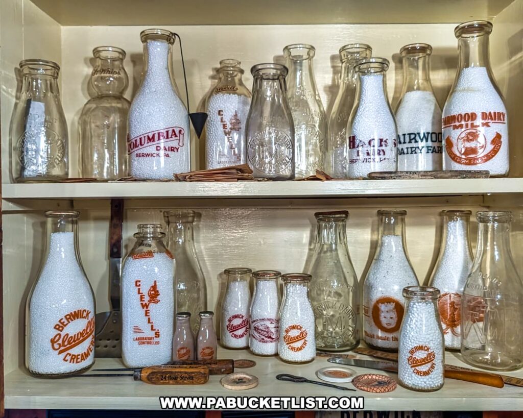 Collection of vintage Berwick dairy bottles on display at the Berwick Historical Society Museum in Columbia County, PA, featuring embossed and painted glass bottles from local creameries and dairies, along with milk caps and delivery tools showcasing the region’s agricultural heritage.