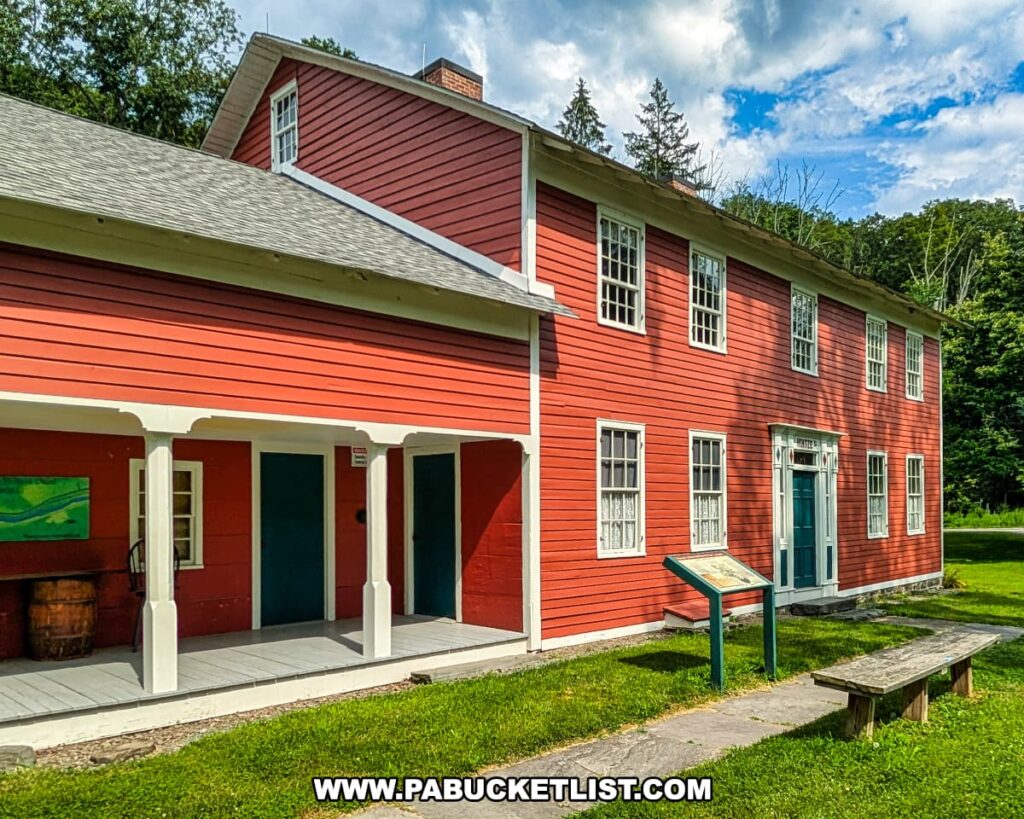 The historic red Daniels Farmhouse at the D\&H Canal Park in Wayne County, Pennsylvania, featuring white trim, multiple paned windows, a covered porch, and an interpretive sign in front on a sunny day.