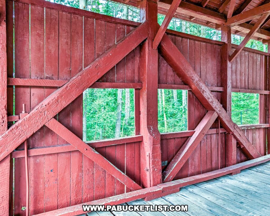 Close-up interior view of the McClurg Covered Bridge in Washington County, Pennsylvania, highlighting the red wooden Kingpost truss construction and square window openings overlooking the surrounding trees.