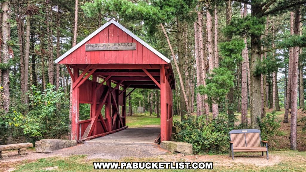 McClurg Covered Bridge in Washington County, Pennsylvania, a small red wooden Kingpost truss bridge built in 1880, surrounded by tall pine trees with a park bench nearby.