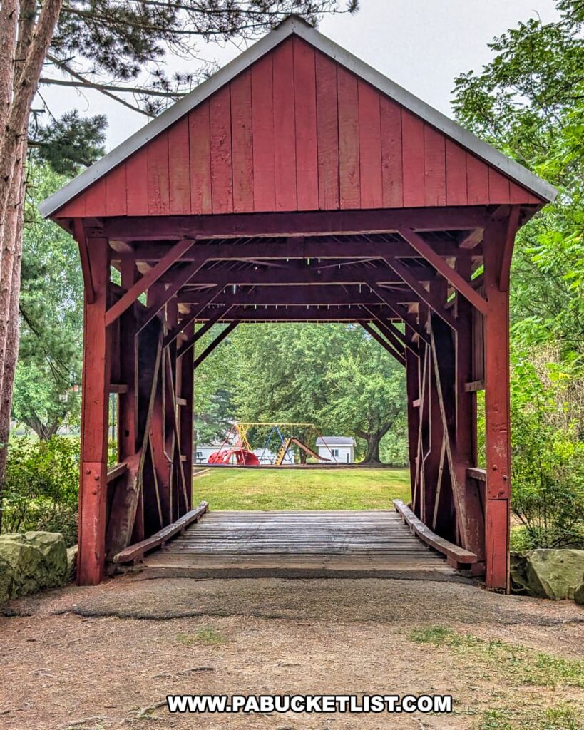 View through the McClurg Covered Bridge in Washington County, Pennsylvania, showing the red wooden structure with a playground and trees visible beyond the bridge.
