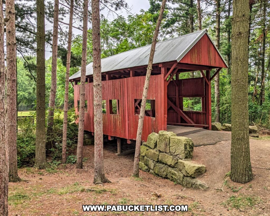 Side view of the McClurg Covered Bridge in Washington County, Pennsylvania, a small red wooden Kingpost truss bridge built in 1880, surrounded by tall trees in Hanover Township Park.