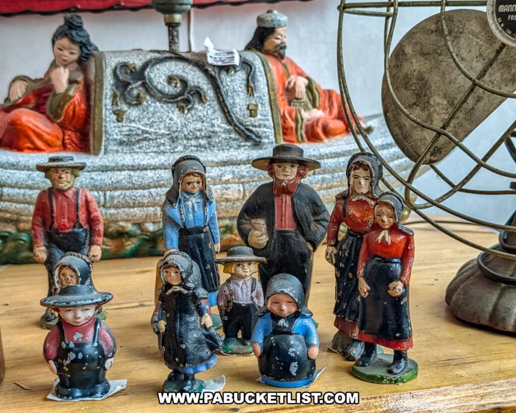 Close-up of vintage painted cast iron figurines depicting Amish men, women, and children displayed on a wooden table at Plains Antiques in Luzerne County, PA, with additional antique decor visible in the background of this two-level multi-vendor antique shop near Wilkes-Barre.