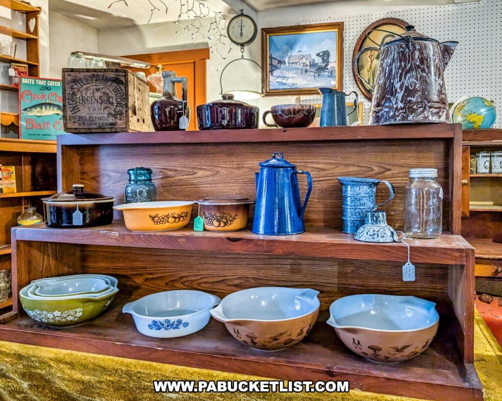 Wooden shelves at Plains Antiques in Luzerne County, PA, displaying a collection of vintage kitchenware including Pyrex mixing bowls, enamelware coffee pots, stoneware crocks, glass jars, and other retro dishware in this two-level multi-vendor antique shop near Wilkes-Barre.