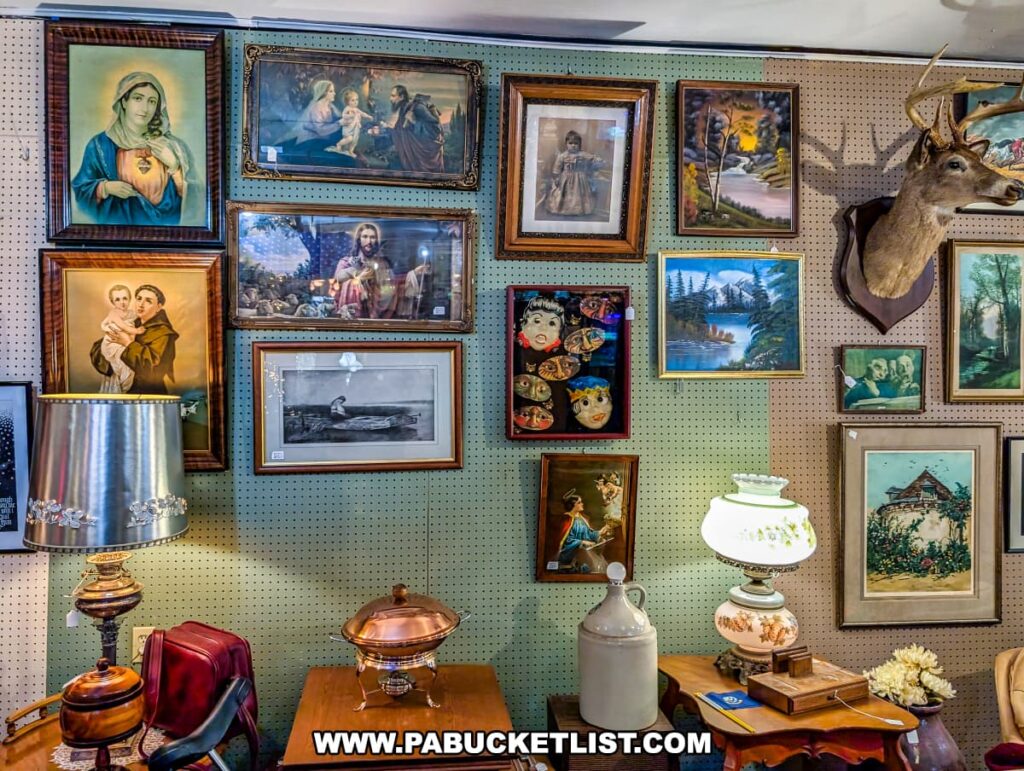 Wall display at Plains Antiques in Luzerne County, PA, featuring framed religious and landscape artwork, vintage lamps, a mounted deer head, and assorted decorative items in this two-level multi-vendor antique shop near Wilkes-Barre.