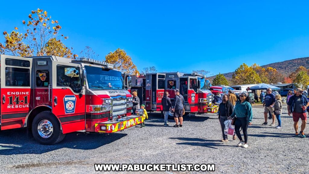 Visitors walk past bright red Howard Fire Company trucks on display at the Punkin Chunkin Fall Festival at Bald Eagle State Park in Centre County, PA, with autumn foliage and vendor tents in the background.