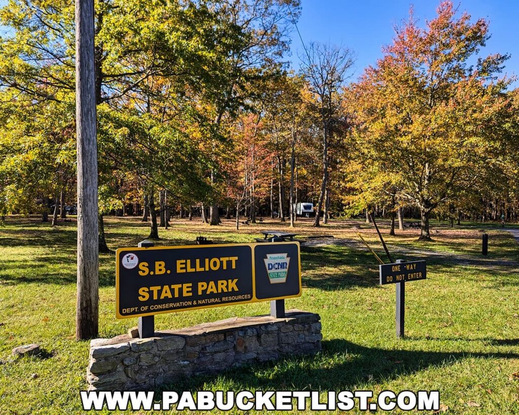 Entrance sign for SB Elliott State Park in Clearfield County, Pennsylvania, set against a backdrop of colorful autumn foliage and a clear blue sky.