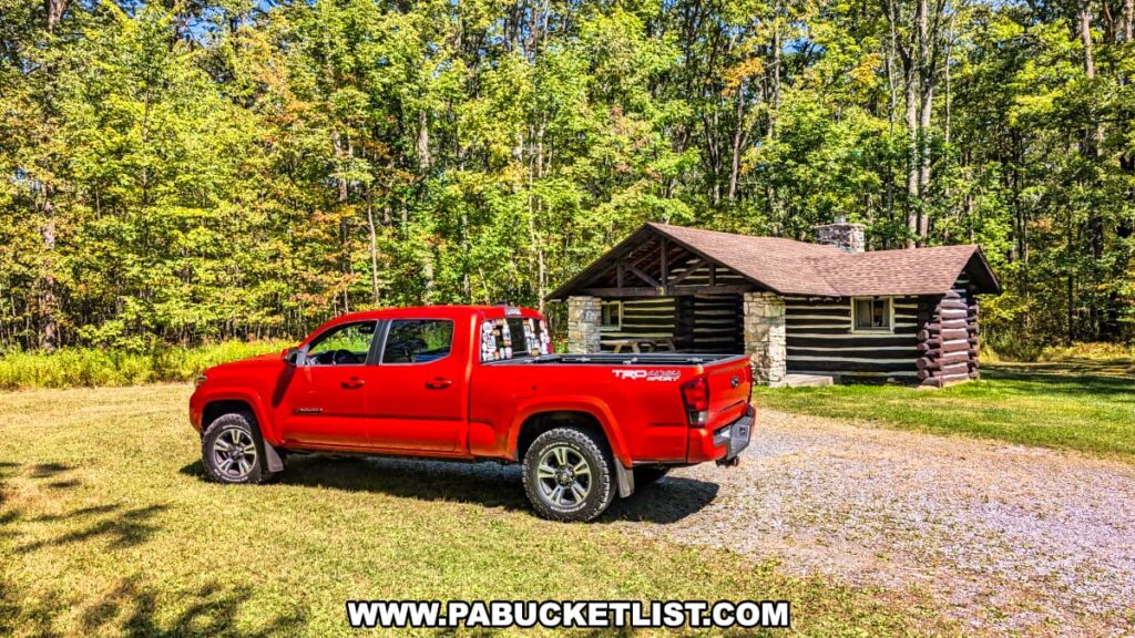 Rustic log cabin built by the Civilian Conservation Corps at SB Elliott State Park in Clearfield County, Pennsylvania, with a red pickup truck parked in front and dense green forest in the background.
