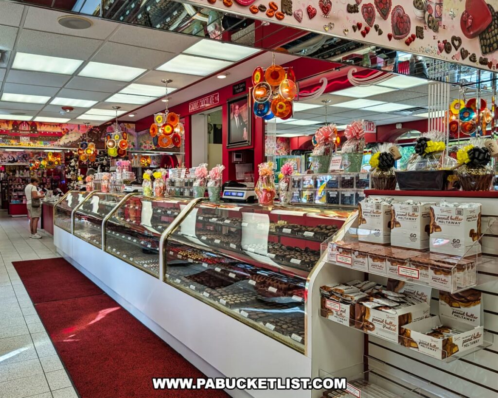 Interior view of Sarris Candies’ Chocolate Factory and Ice Cream Parlour in Canonsburg, PA, showcasing long glass display cases filled with assorted chocolates, shelves stocked with peanut butter meltaways, colorful hanging light fixtures, and a cheerful, candy-themed decor.