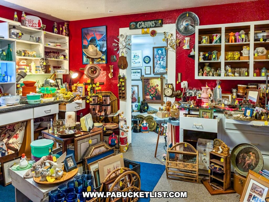 Colorful vendor space inside Vintage Secrets Antiques in Canonsburg, Washington County, PA, featuring shelves and tables filled with vintage glassware, kitchenware, framed art, clocks, figurines, and eclectic collectibles against a bold red wall.