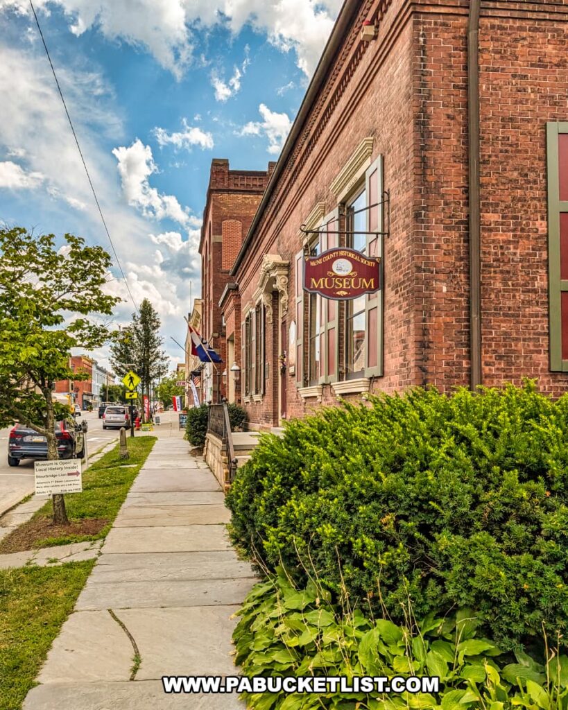 Exterior view of the Wayne County Historical Society Museum in Honesdale, Pennsylvania, housed in the former 1860 Delaware & Hudson Canal Company headquarters building, with a museum sign hanging above the sidewalk along Main Street.
