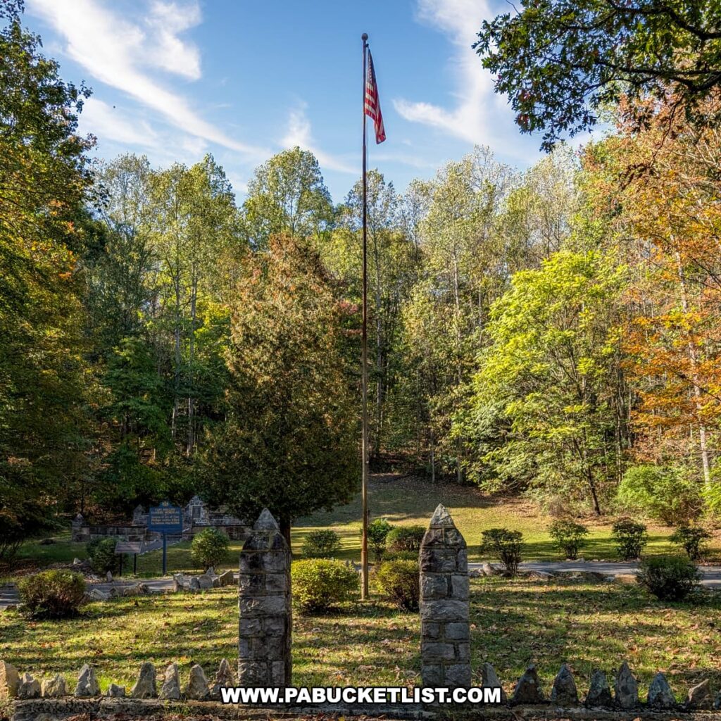 American flag flying on a tall flagpole above the Captain Phillips’ Rangers Memorial in Bedford County, Pennsylvania, surrounded by trees with early autumn foliage under a bright blue sky with wispy clouds.