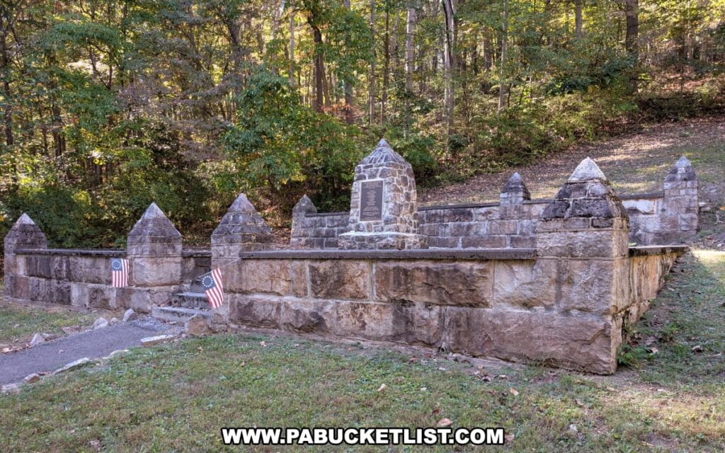 Front view of the Captain Phillips’ Rangers Memorial in Bedford County, Pennsylvania, featuring a stone monument with a bronze plaque and low surrounding wall adorned with early American flags, set against a wooded hillside.