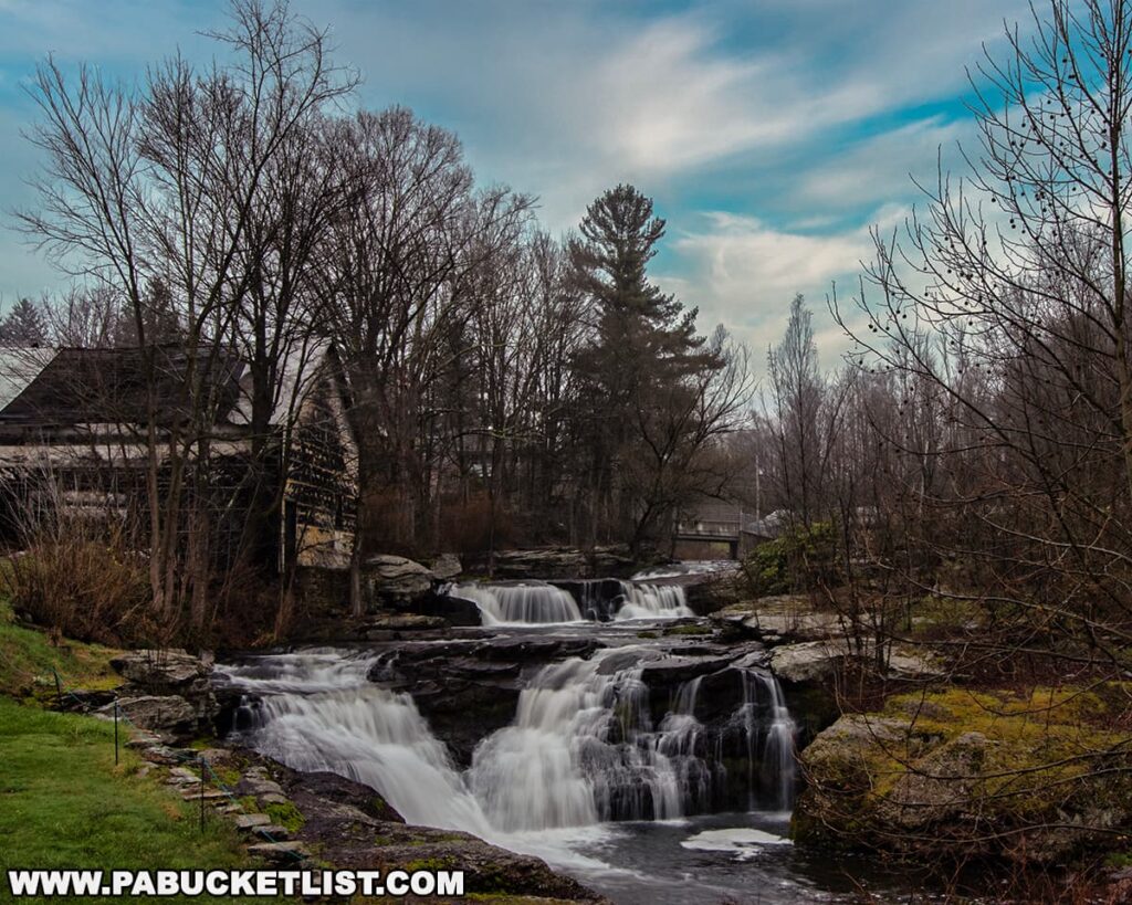 Carley Brook Falls in Wayne County, PA, a scenic 20-foot multi-tiered waterfall flowing over layered rock formations surrounded by early spring trees, with an old weathered building and small bridge visible near the top of the falls along Route 6 near Honesdale.