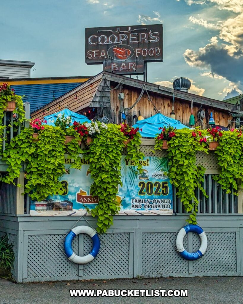 The exterior of Cooper’s Seafood House in Scranton, Pennsylvania, featuring a rustic nautical-themed facade with lush greenery, life rings, colorful flowers, and a vintage neon sign above the outdoor dining area.