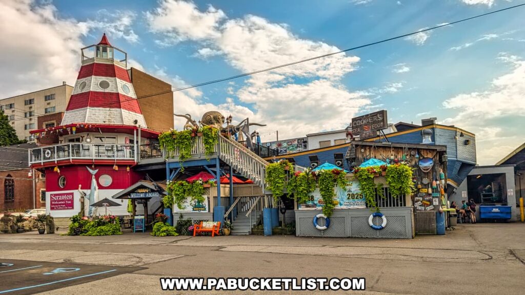 A wide view of Cooper’s Seafood House in Scranton, Pennsylvania, showcasing its red-and-white lighthouse tower, nautical-themed decor with life rings and hanging plants, and outdoor dining area beneath bright umbrellas on a sunny day.