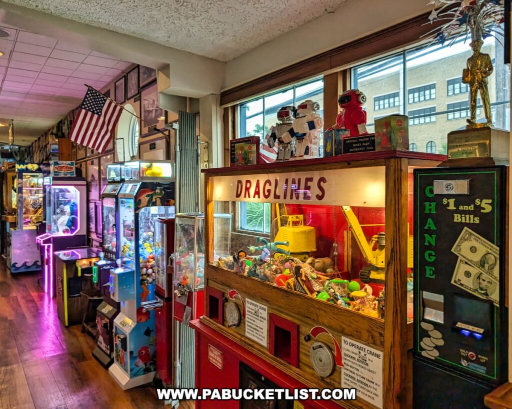 A colorful arcade area inside Cooper’s Seafood House in Scranton, Pennsylvania, featuring vintage and modern claw machines, a change dispenser, and a display of nostalgic toys beneath an American flag and framed nautical decor.