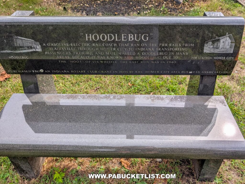 Granite memorial bench along the Hoodlebug Trail in Indiana County, Pennsylvania, engraved with the history of the “Hoodlebug,” a gasoline-electric railcoach that once ran on the Pennsylvania Railroad line from Blairsville through Homer City to Indiana. The inscription explains that the coach transported passengers, freight, and mail, earning its nickname from the “hoot” of its whistle before its final run in 1940. Small etched images of the railcar and the Homer City station decorate each end of the bench, which sits on a grassy area beside the 10-mile trail that now follows the former railroad route.