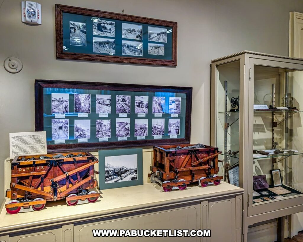 Coal mining and railroad exhibit inside the Lackawanna Historical Society Museum in Scranton, Pennsylvania. The display features two detailed wooden mine car models labeled for regional railroads, surrounded by framed historic photographs of rail lines and mining operations, along with glass cases containing artifacts that highlight the area’s industrial and transportation heritage.