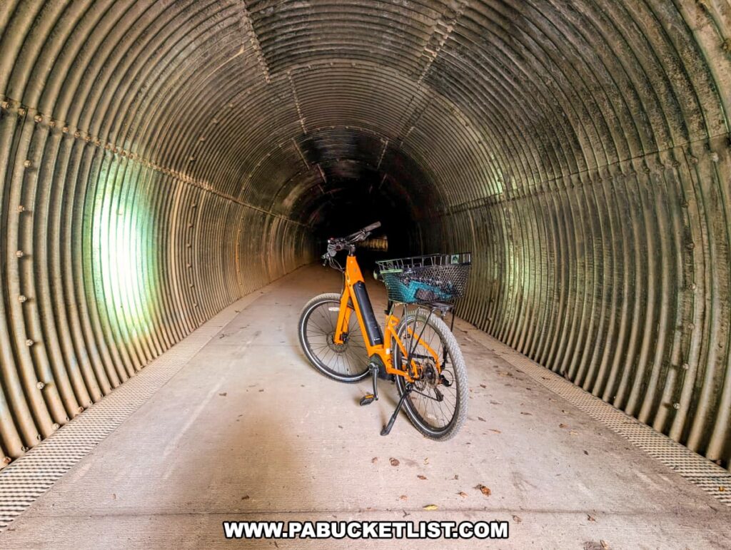 An orange bicycle with a black basket is parked inside the curved, metal-lined Poe Paddy Tunnel along the Penn’s Creek Path in Bald Eagle State Forest, illuminated by faint light filtering from the tunnel’s distant openings.