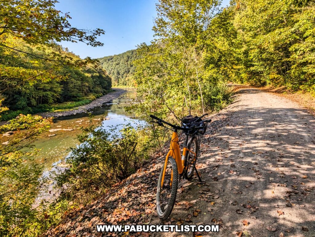 Orange bicycle parked on the gravel path of the Redbank Valley Rail Trail overlooking Redbank Creek, with calm waters reflecting the surrounding forested hills on a sunny day.