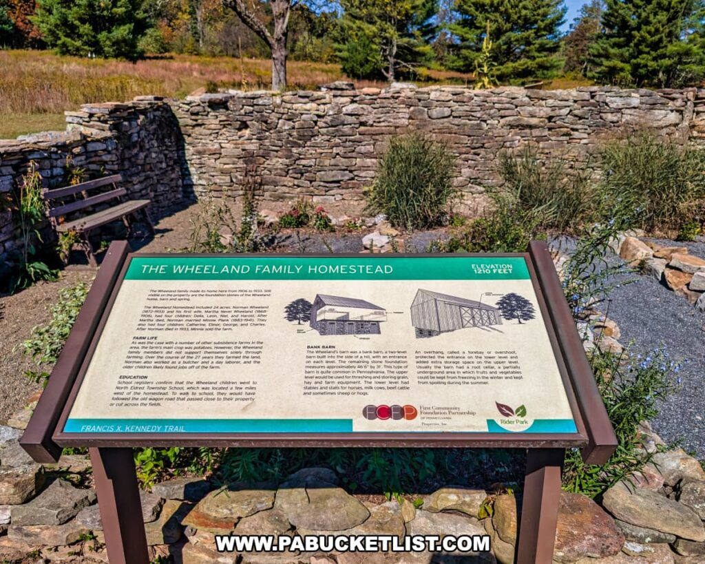 Informational sign for the Wheeland Family Homestead at Rider Park in Lycoming County, Pennsylvania, describing early farm life, education, and the design of a traditional bank barn, with stone foundation ruins and benches visible in the background.