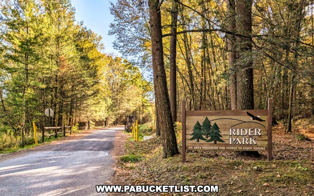 Entrance sign for Rider Park in Lycoming County, Pennsylvania, reading “An area preserved for people to enjoy nature,” positioned beside a quiet tree-lined road surrounded by golden autumn foliage.
