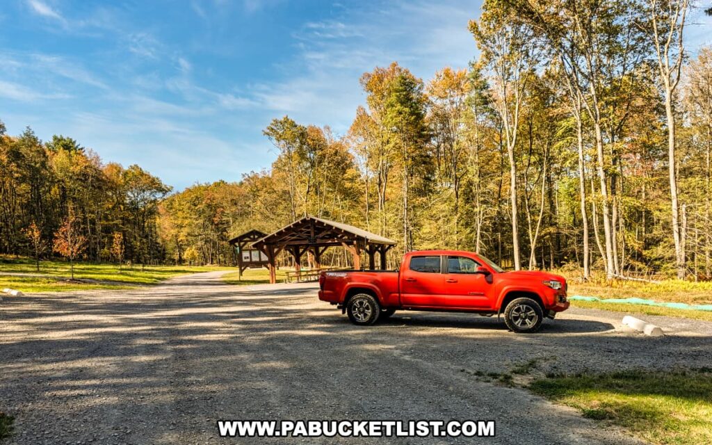 Parking area at Rider Park in Lycoming County, Pennsylvania, featuring a bright red pickup truck parked near a wooden picnic pavilion and trailhead kiosk surrounded by colorful autumn trees under a clear blue sky.