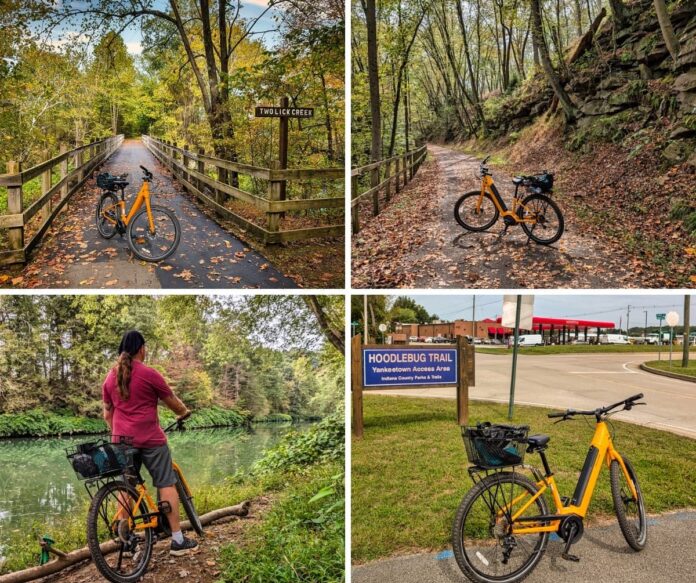 Collage of four photos taken along the Hoodlebug Trail in Indiana County, Pennsylvania. The top left image shows a bright yellow bicycle on a bridge over Two Lick Creek surrounded by autumn trees. The top right image features the same bicycle on a leaf-strewn trail bordered by rocky cliffs and forest. The bottom left image shows a cyclist pausing beside calm green water, framed by trees along the creek. The bottom right image depicts the bicycle parked near a sign for the Hoodlebug Trail Yankeetown Access Area, with a red-roofed Sheetz gas station in the background. The 10-mile Hoodlebug Trail follows the former Pennsylvania Railroad’s Indiana Branch, once traveled by the self-propelled “Hoodlebug” passenger coach.