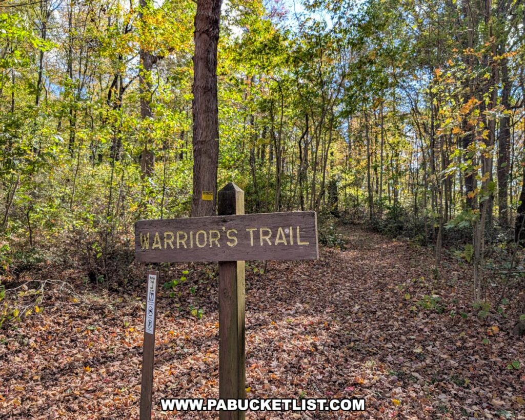 A wooden sign marked “Warrior’s Trail” stands at the entrance to a leaf-covered forest path surrounded by colorful autumn foliage at Warriors Path State Park in Bedford County, Pennsylvania.