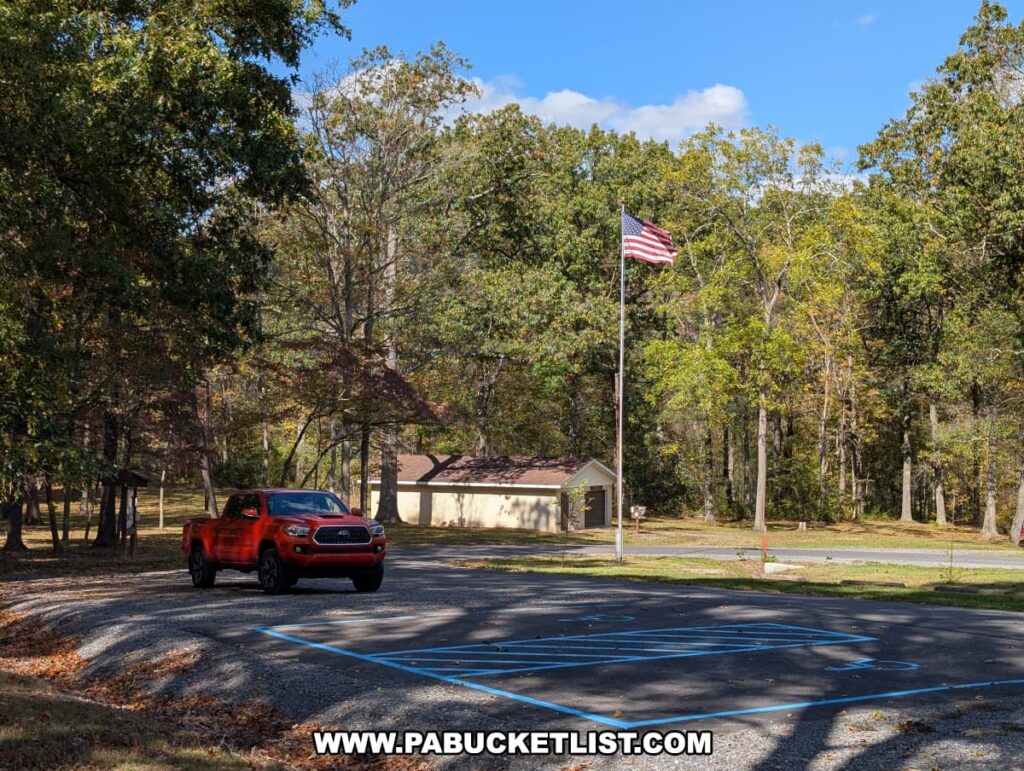 A red pickup truck is parked in a lot near an American flag and a small picnic pavilion at Warriors Path State Park in Bedford County, Pennsylvania, surrounded by trees with early fall foliage under a bright blue sky.