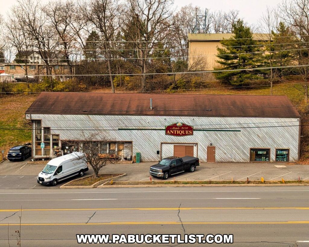 Apple Hill Antiques near State College shown from across the road, featuring a long rustic building with a weathered exterior, a sloped brown roof, and several parked vehicles in front on an overcast late-fall day.