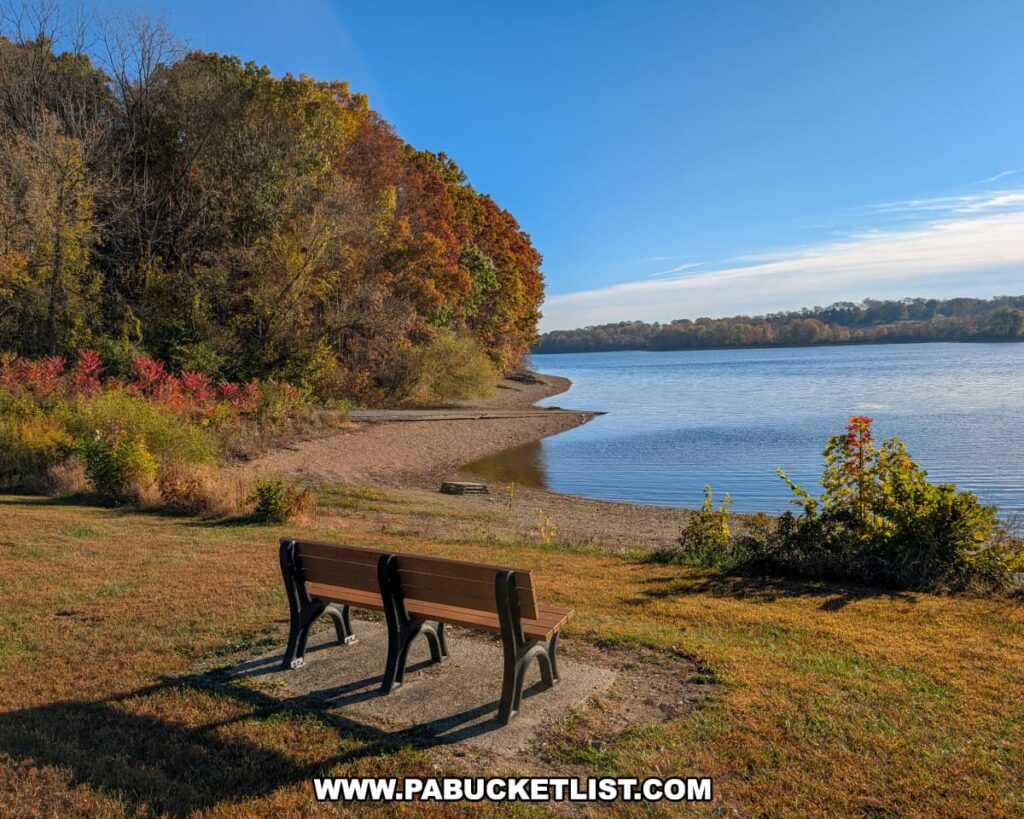 Two benches overlook the calm waters of Lake Marburg at Codorus State Park in York County, Pennsylvania, surrounded by colorful autumn foliage and a clear blue sky.