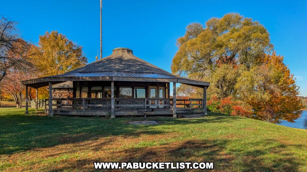 A round wooden pavilion-style building with large windows stands near the water’s edge at Codorus State Park in York County, Pennsylvania, surrounded by colorful autumn trees under a clear blue sky.