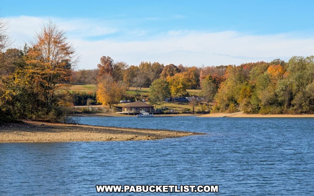 A view across Lake Marburg at Codorus State Park in York County, Pennsylvania, shows the marina building nestled among colorful autumn trees on the opposite shore under a clear blue sky.